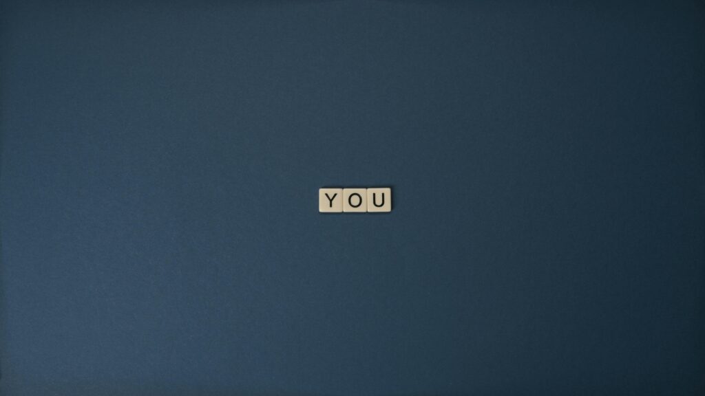 Flat lay of Scrabble letters spelling 'YOU' on a blue background, perfect for conceptual themes.